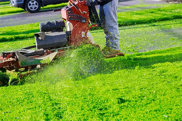 man riding a large red lawnmower as it blows cut grass out the side of the mower