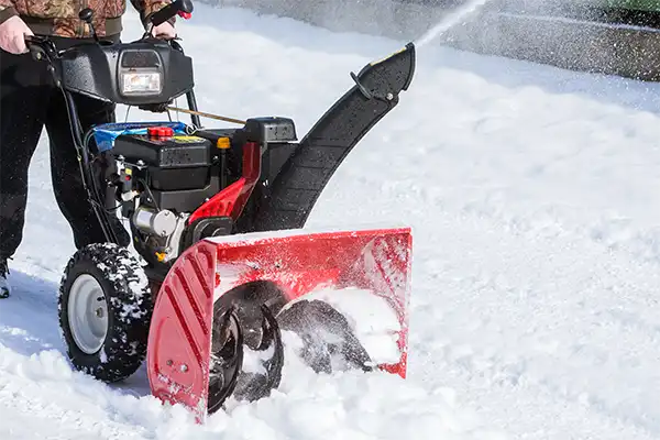red snow blower being pushed across snow covered street and expeling plumes of snow